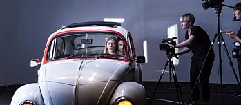 A pla takes place onstage. Actors sit inside a car while being filmed from outside the car.