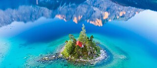 Eine sehr kleine Insel in einem Bergsee, die Berge spiegel sich im Wasser