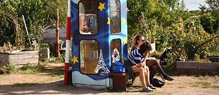 Zwei junge Menschen sitzen vor einem Bücherschrank, der in den Farben Europas bemalt ist.