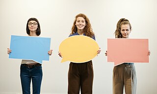 Drei junge Frauen halten leere Sprechblasen.