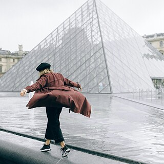 Eine Frau balanciert neben Glaspyramide vor dem Louvre in Paris.