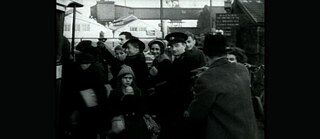 Schwarzweißes Archivbild einer eng gedrängten Gruppe von Mensche auf einem Bahnhof