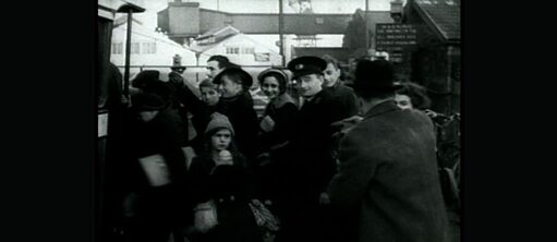 Schwarzweißes Archivbild einer eng gedrängten Gruppe von Mensche auf einem Bahnhof