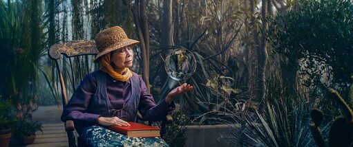 Filmstill aus „Everything will change”: eine Frau sitzt in einem Wald und beobachtet eine Kristallkugel