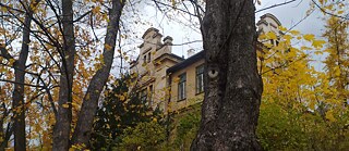 Photo is showing the view from below on a building of the psychiatric clinic in Prague-Bohnice through trees and bushes with autumn leaves. 