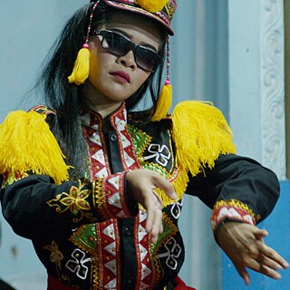 Eine Darstellerin in einem Kostüm, das eine Mischung aus moderner Militäruniform und traditioneller thailändischer Kleidung und Sonnenbrille ist, tanzt 