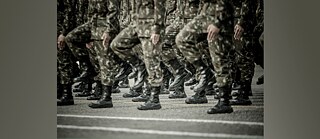 Photo is showing marching soldiers, only their legs and upper bodies are visible. 