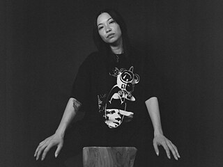 Portrait of Felicia Chen sitting on a chair wearing a cartoon t-shirt  © Sina Lesnik Felicia Chen b&w 2