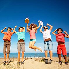 Eine Gruppe von vier Jungen und einem Mädchen befinden sich am Strand, sich springen und schreien freudig für das Foto