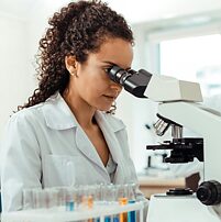 a scientist in a white coat looks into a microscope