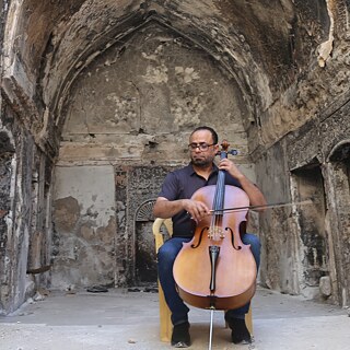 Ein Mann spielt Cello vor der Kulisse eines zerstörten Gebäudes in Mosul