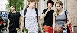 Sylvan in Deutschland. Er ist mit Freunden auf dem Nachhauseweg vom Basketball spielen. Er trägt ein Skateboard unter dem Arm.