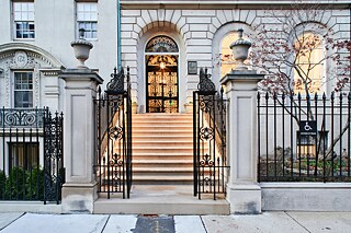 Photo of the front entrance to the Goethe-Institut Boston, depicting a wrought iron fence, two large columns, and a stairway leading to the front doors of the building. 