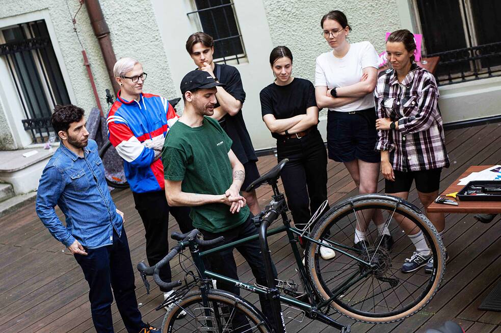 People standing around a bicycle that is been fixed by kola