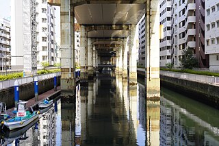 A canal flows quietly beneath a rusty motorway. The silent observer of the city bears witness to the dream of endless progress. The rusty pillars give away how long the motorway has already been part of the cityscape.