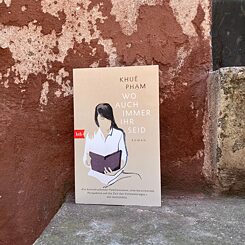 The picture shows the book cover of ‘Wherever you are’, the book is standing on a stone staircase, in the background you can see a brown painted wall from which the colour is peeling.