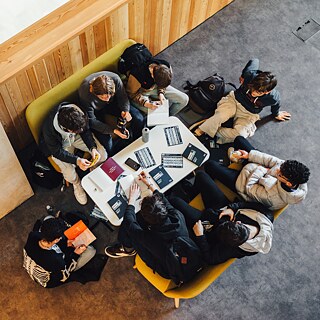 Flera unga elever sitter runt ett bord och läser informationsmaterial.