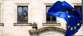 Photo is showing a flag of the EU in front of a building. 