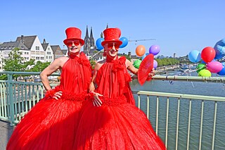 Christopher Street Day (CSD) in Köln, zwei Teilnehmende in roten Kostümen auf einer Rheinbrücke