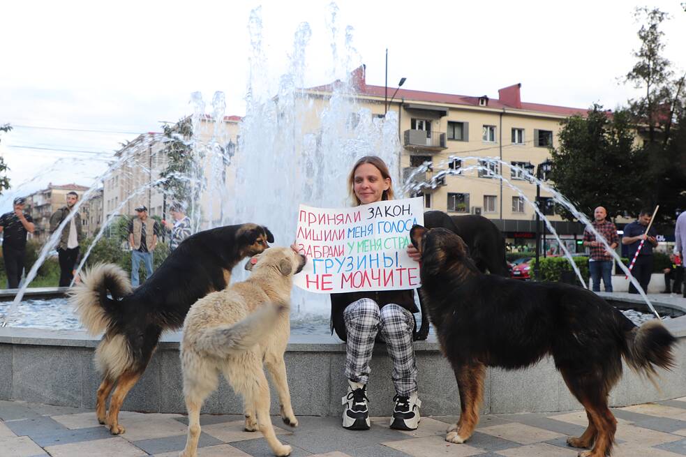 Jevgenija s toulavým psem. V ruce drží transparent „Přijali zákon, zbavili mě volebního práva a vzali mi mou zemi. Gruzínci, nemlčte“.