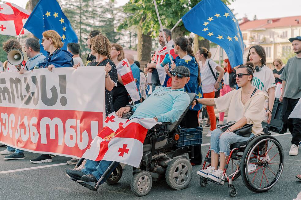 Sofia kann sich keinen elektrischen Rollstuhl leisten, deshalb hält sie sich am Rollstuhl von Ruslan fest, damit sie zusammen mit allen anderen an den Protesten teilnehmen kann.