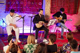 Drei Musiker spielen Instrumente auf einer kleinen Bühne