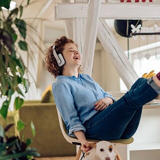 En kvinna med hörlurar sitter bekvämt hemma och lyssnar på en podd.