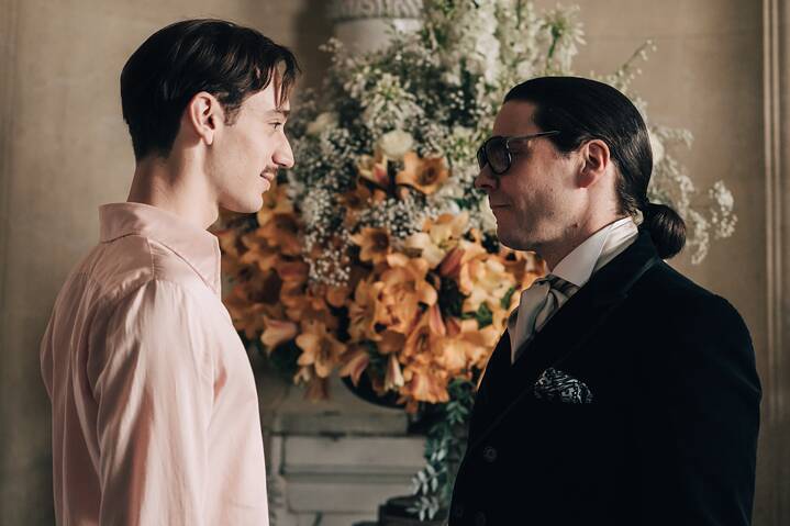 In a scene from the series "Becoming Karl Lagerfeld", Karl Lagerfeld and Jacques de Bascher gaze at each other in front of an opulent bouquet of flowers.