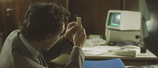 Mann hält einen kleinen Stapel mit Coupons hoch, im Hintergrund ein altmodischer Computer