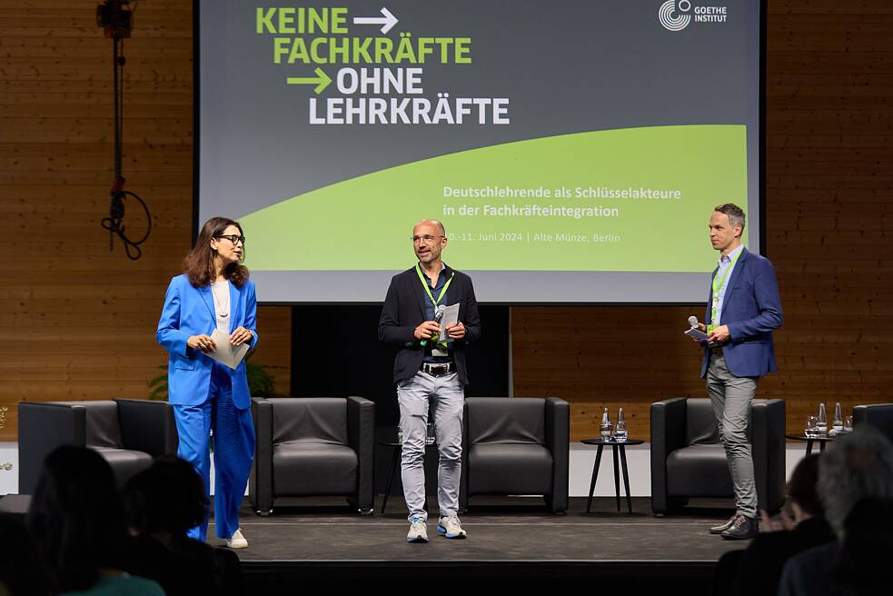Amira El-Ahl (Moderatorin), Christoph Mohr (Bereichsleiter Vernetzungsprogramm) und Jan Sprenger (Bereichsleiter Fortbildungen) stehen auf der Bühne mit dem Titel der Veranstaltung.