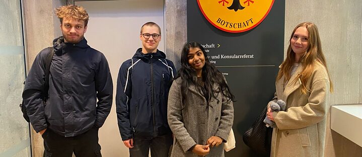 4 Schülerinnen und Schüler stehen vor dem Schild der Deutschen Botschaft in Kopenhagen, sie sind auf dem Weg zu einem Debattierwettbewerb.
