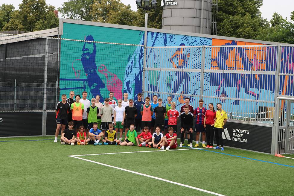 Die Jugendlichen stehen auf dem Fussballfeld an dem Wandgemälde