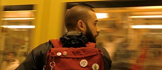 A man with a backpack looks on as a subway train passes by