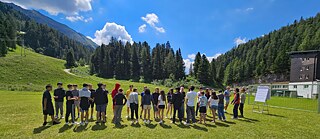 Jugendliche stehen in einer Reihe auf einer Wiese, im Hintergrund die Alpen.
