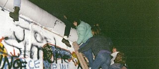 Young women climbing the Berlin Wall in the middle of the night.