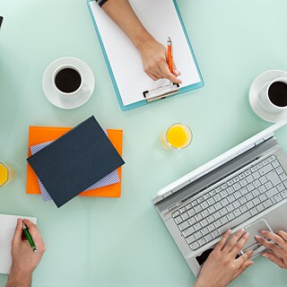 Die Kursteilnehmer bei der Gruppenarbeit. Sie schreiben ihre Notizen auf Schreibblöcke und an Laptops. Blick von oben.