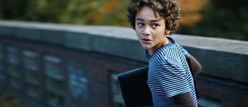 En scene fra filmen "Lærerværelset", et barn løber over en bro og ser sig ængsteligt tilbage med en bærbar computer under armen.