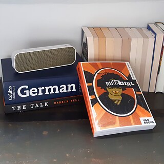 Die Bücher 'Rude Girl' und 'The Talk' liegen neben einem Wörterbuch und weiteren Büchern auf einem Lautsprecher