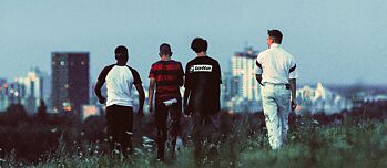 Scene billedet fra filmen "Sonne und Beton" viser fire unge drenge bagfra. De går over en eng i skumringen, og i det fjerne kan man se højhuse i Berlin.
