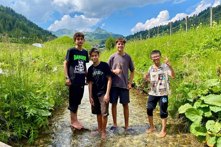 Vier Jugendliche stehen mit den nackten Füßen in einem Bergbach und sind fröhlich.