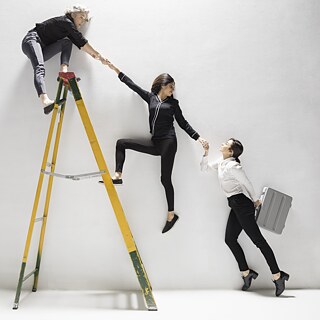 Drei Geschäftsfrauen helfen sich gegenseitig beim ersteigen einer Leiter.