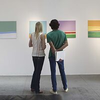 two people from behind who are looking at modern paintings in a gallery