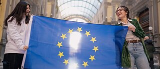 Two young persons holding an eu flag and smiling at each other happily