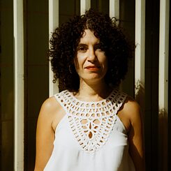 The portrait picture of Maha El Hissy shows a woman with black, chin-length curls. She is wearing a white top with lace and the picture is taken in front of a wall or fence.