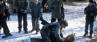 Zwei Jungen raufen sich im Schnee, fünf weitere stehen um sie herum.