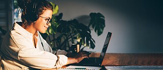 A person wearing headphones and glasses, working on a laptop in a warmly lit room with plants in the background. © © Goethe-Institut Explanatory videos