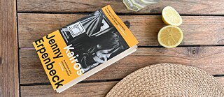 The book 'Kairos' lies next to a straw hat and a glass of lemonade on a table.