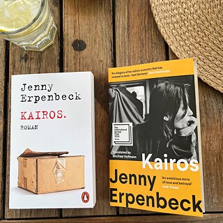 The book 'Kairos' and its translated version by Michael Hofmann are lying next to a straw hat and a glass of lemonade on a table.