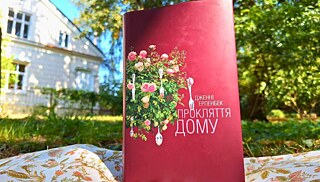 Книжка Дженні Ерпенбек "Прокляття дому" стоїть на траві, на задньому плані сад та будинок