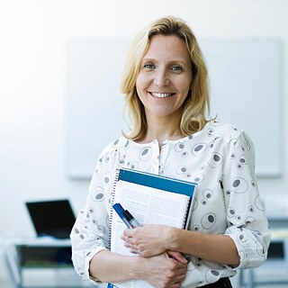 Lehrerin im Klassenzimmer, mit Schreibheften in der Hand.